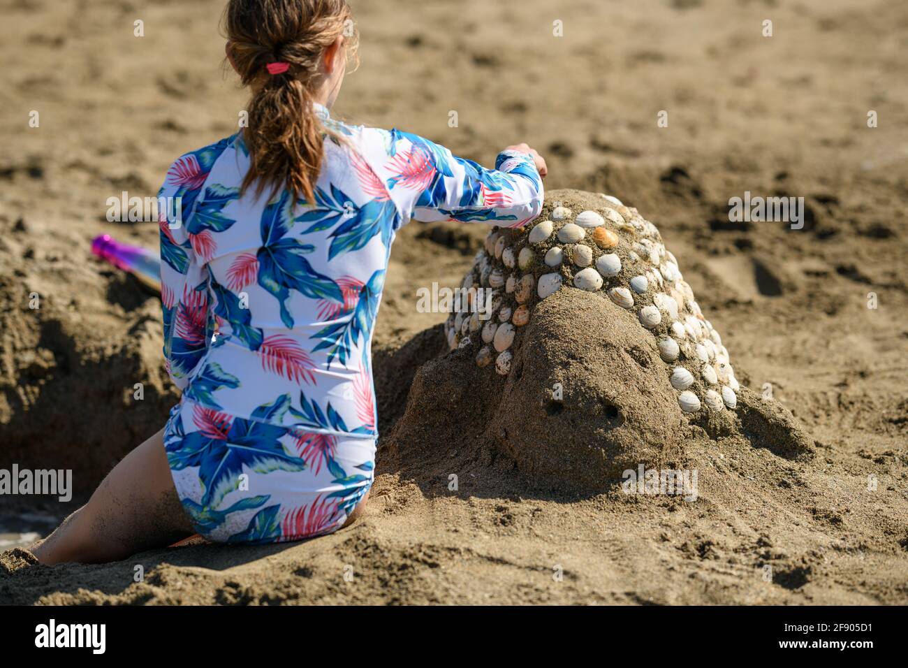 Rear view of a girl sitting on the beach building a sand sculpture with seashells, Ireland Stock Photo