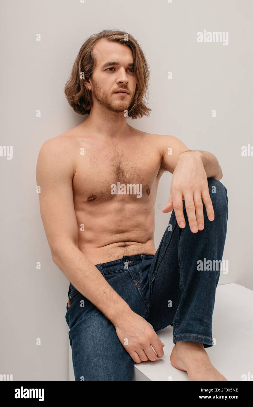 Portrait of a handsome shirtless man in jeans sitting on a table Stock Photo