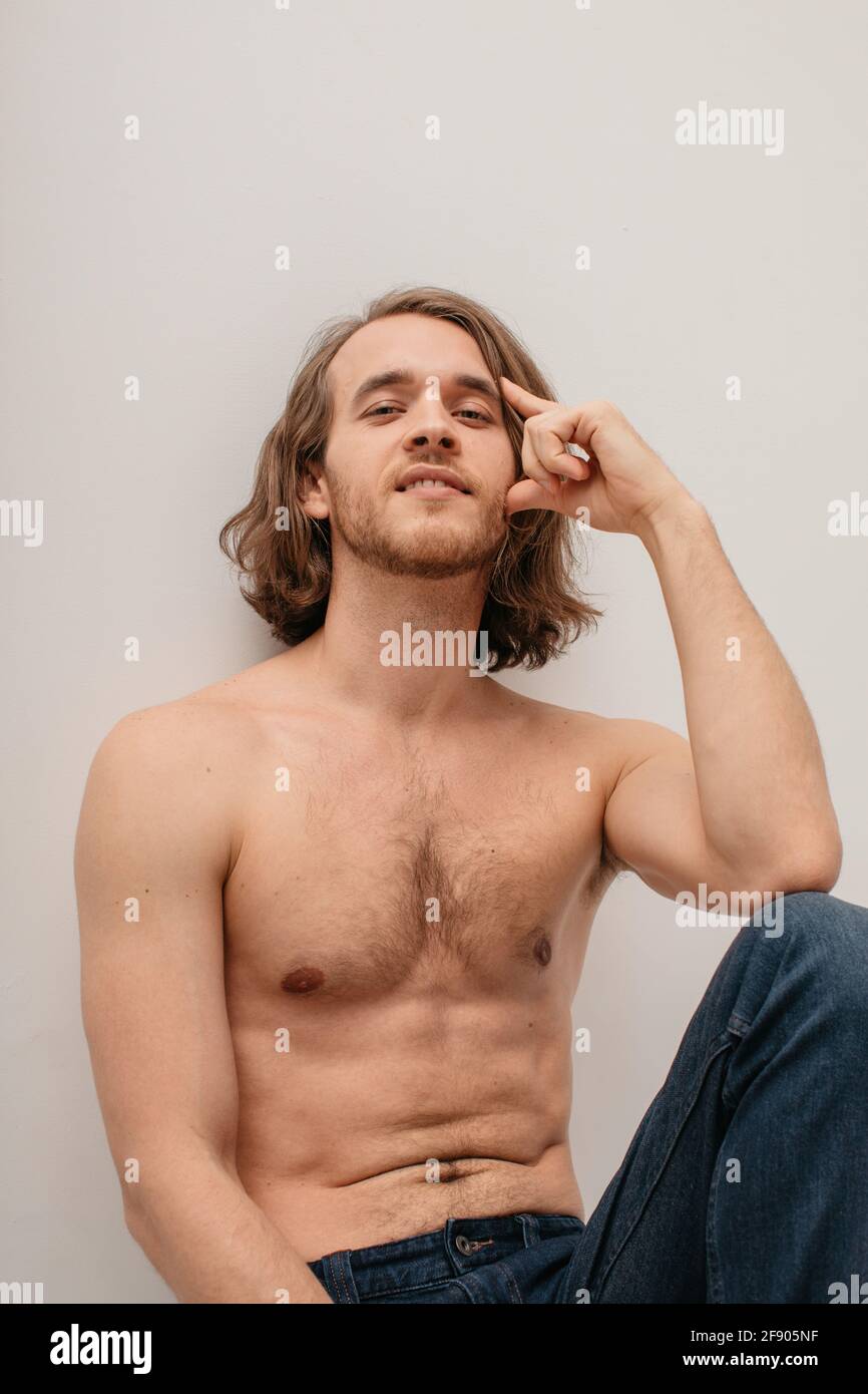 Portrait of a handsome shirtless man in jeans sitting on a table Stock Photo