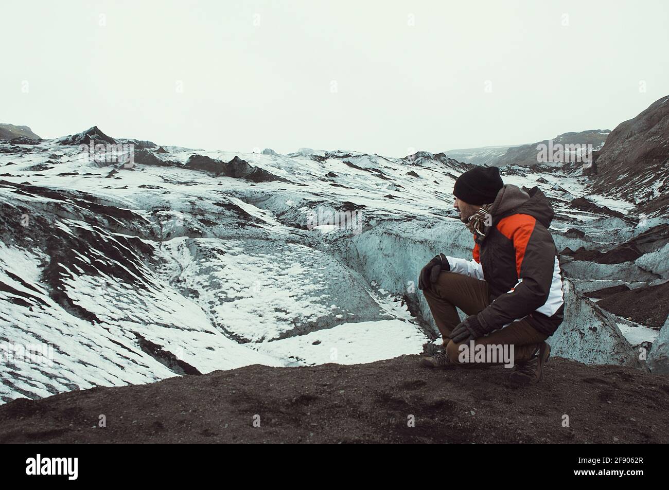 Man kneeling on rocks looking at winter landscape, Iceland Stock Photo ...