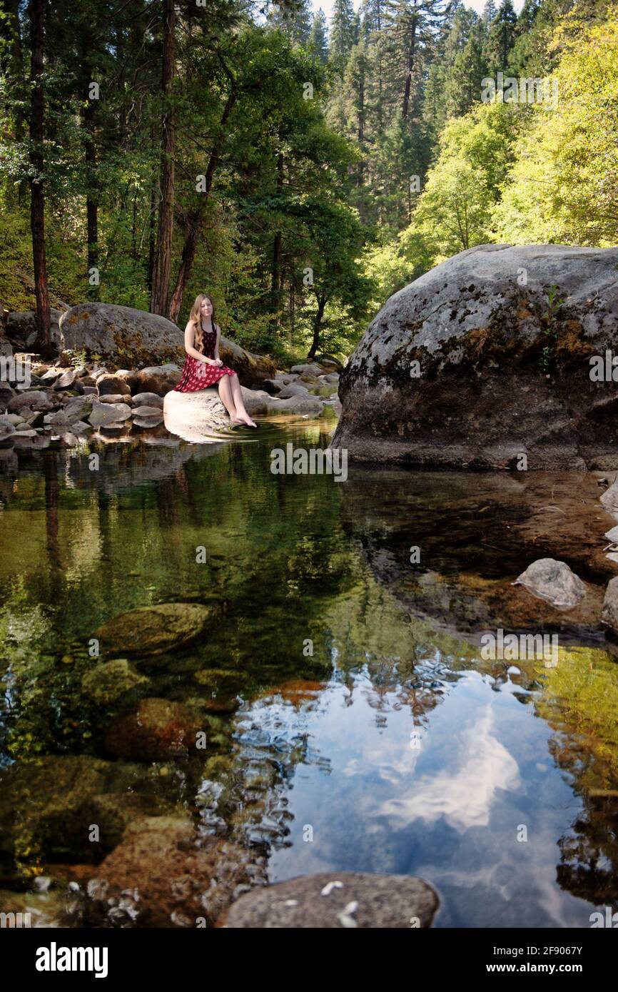 Young woman sitting on a rock by a pond near Lemolo Lake, Oregon, USA Stock Photo