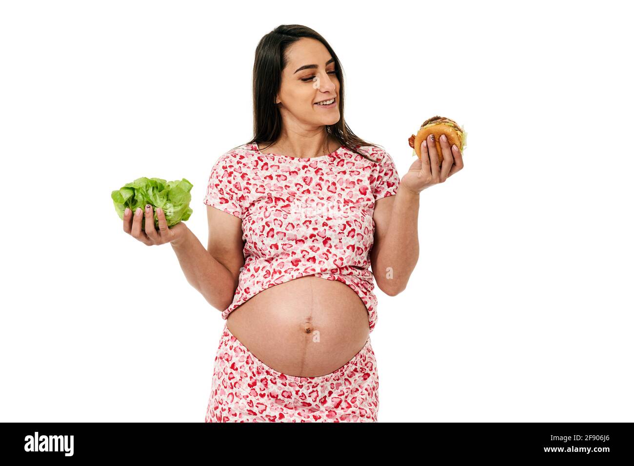 Pregnant woman choosing between a lettuce and a burger, isolated on white background Stock Photo