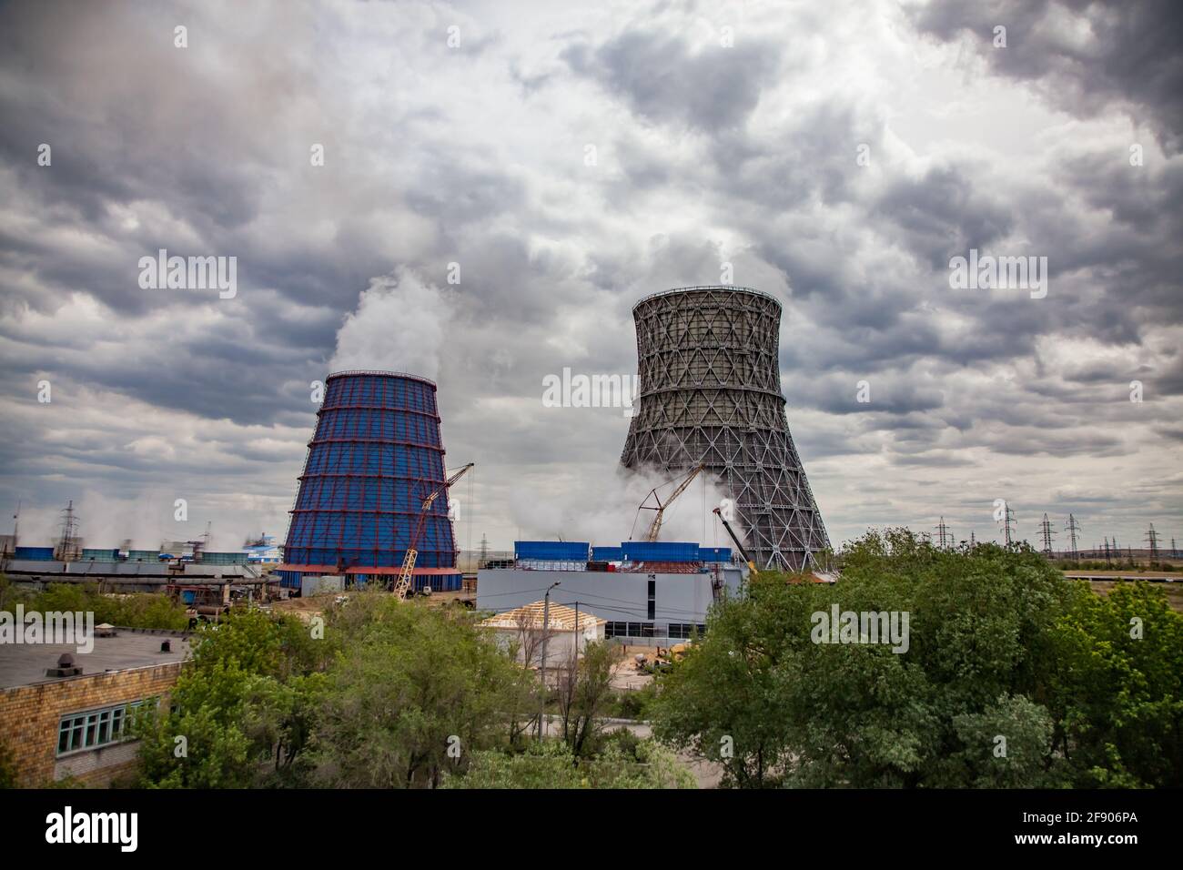 Heat electric plant panoramic view. Cooling towers on background. Green trees. Yellow mobile cranes, grey cloudy sky. Karaganda, Kazakhstan. Stock Photo
