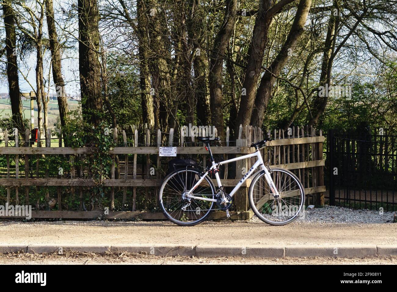 A white bike chained to a wooden fence, next to a sign that says 'Car thieves operate here'. UK countryside setting. Stock Photo