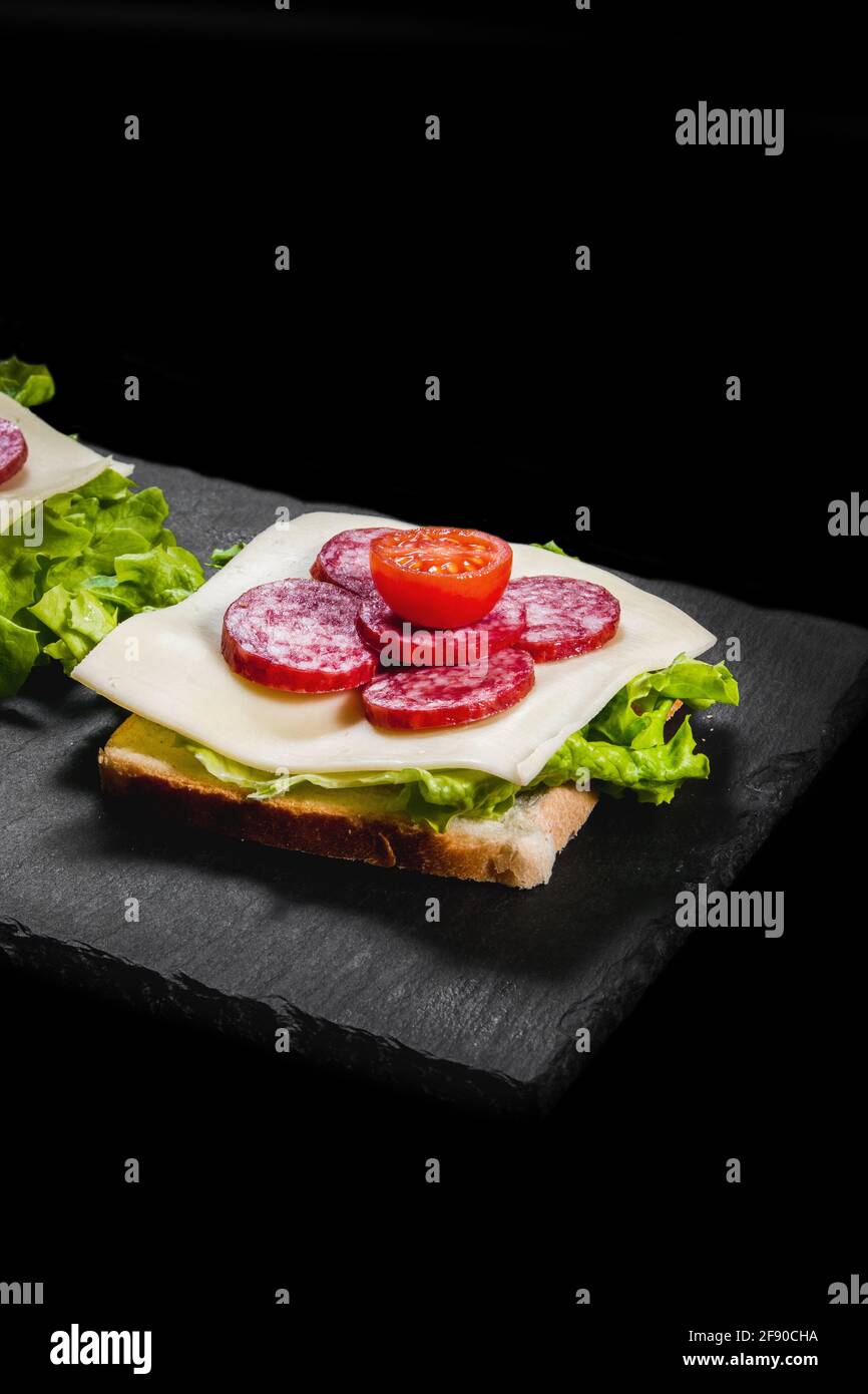 Breakfast sandwiches with dry meat, cheese and lettuce on a black plate Stock Photo