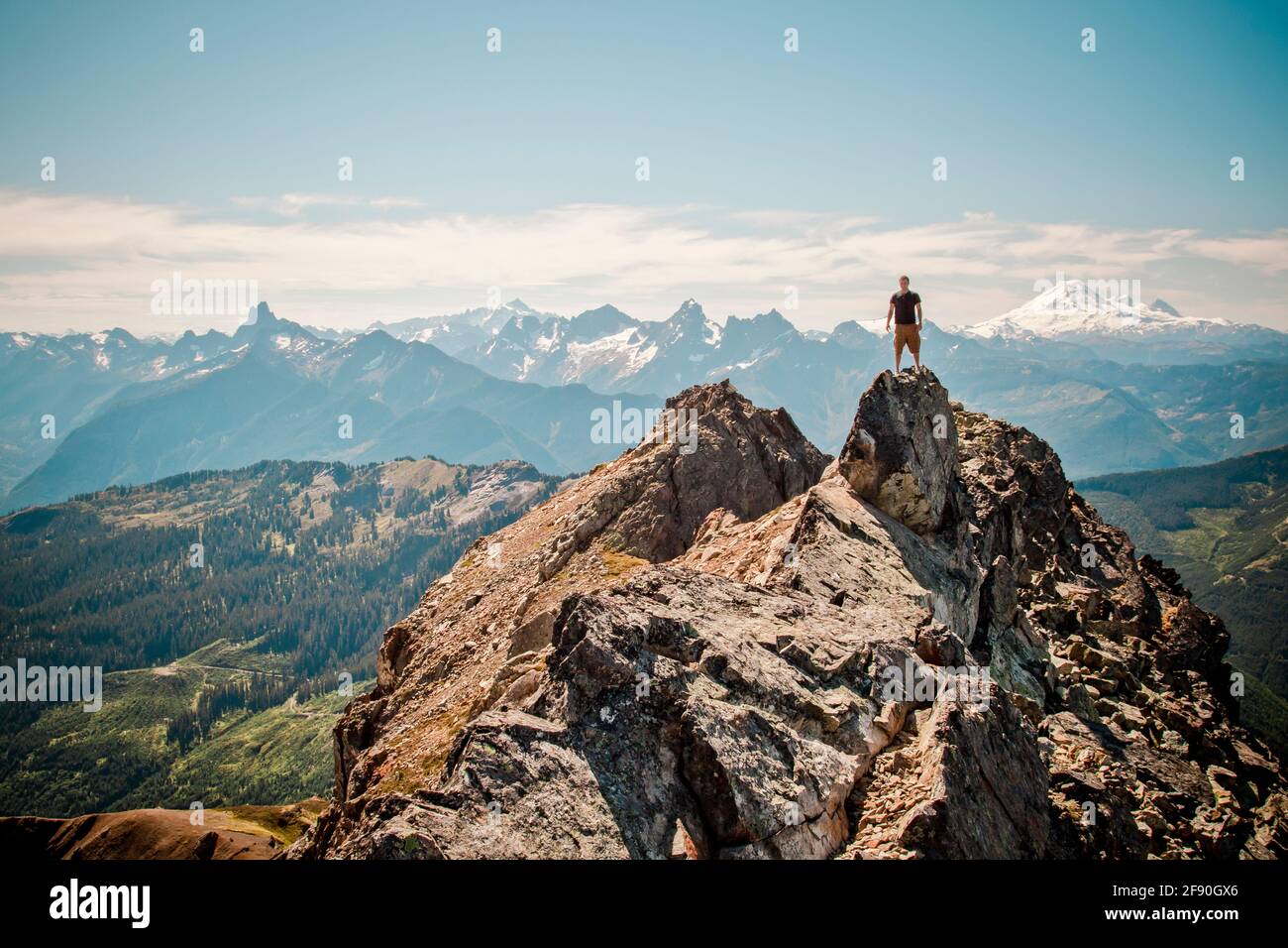 Hiker stands on summit of mountain with scenic view behind. Stock Photo