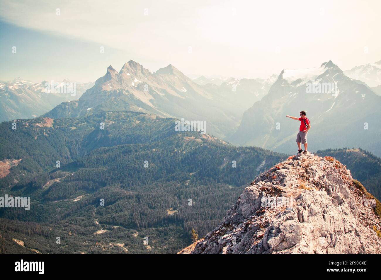 Hiker pointing across valley from rocky mountain summit Stock Photo