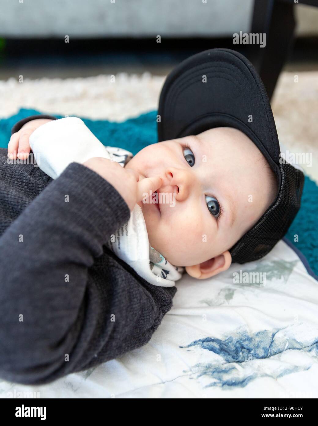 Curious baby boy laying down wearing baseball cap. Stock Photo