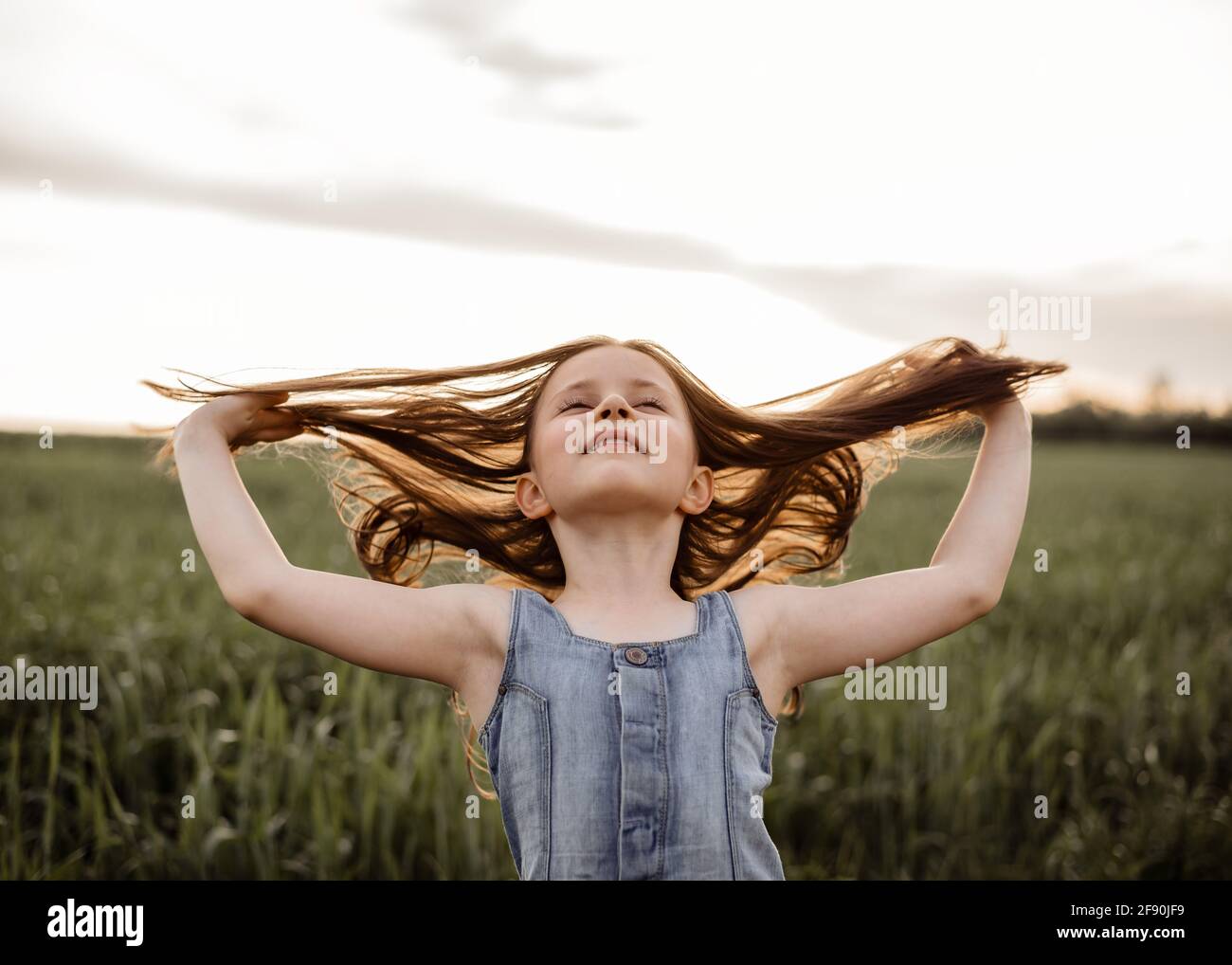 Happy 5 years old girl in a green wheat field with long hair at sunset Stock Photo