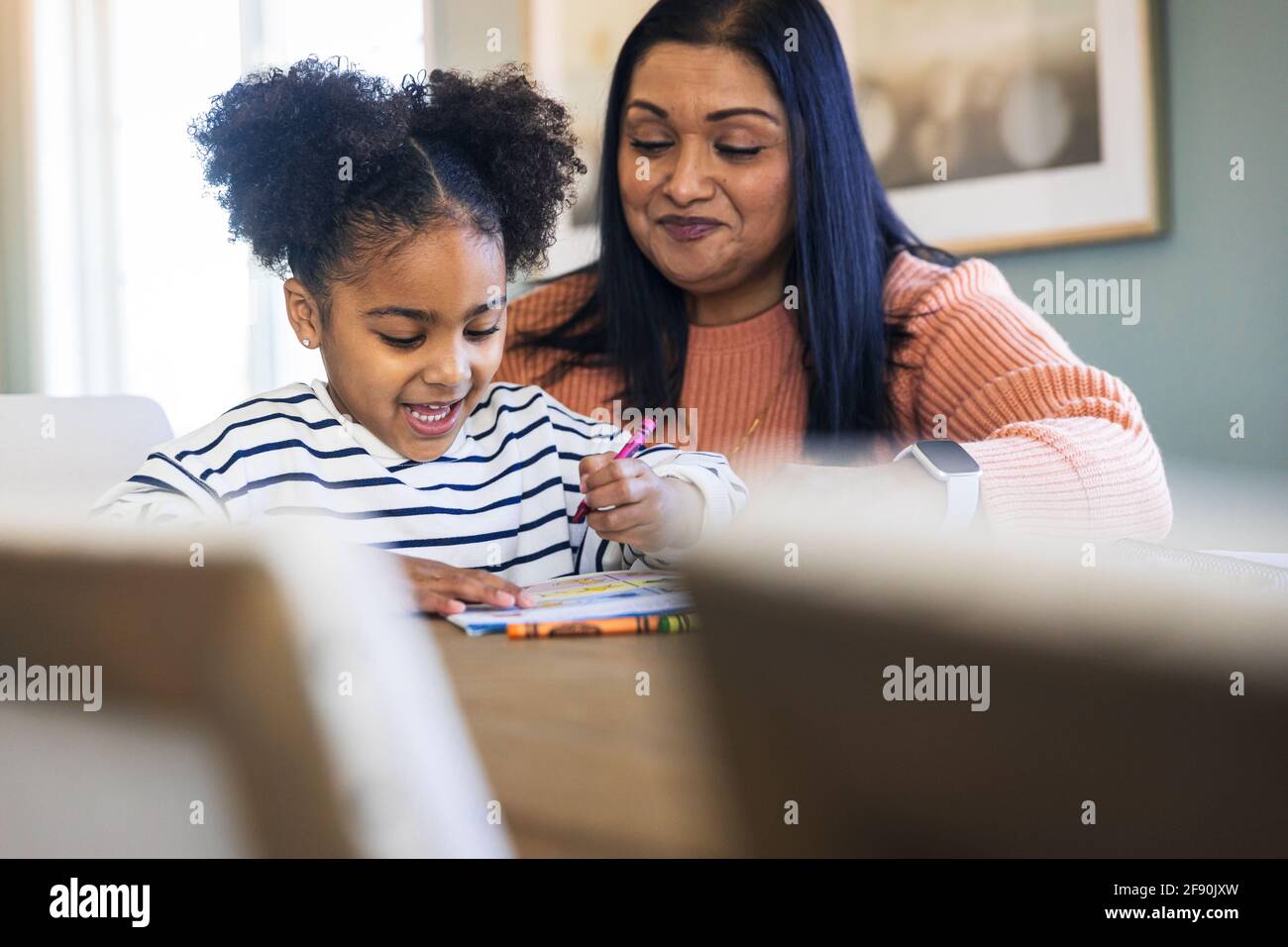 Smiling grandmother guiding granddaughter coloring with crayons in book Stock Photo