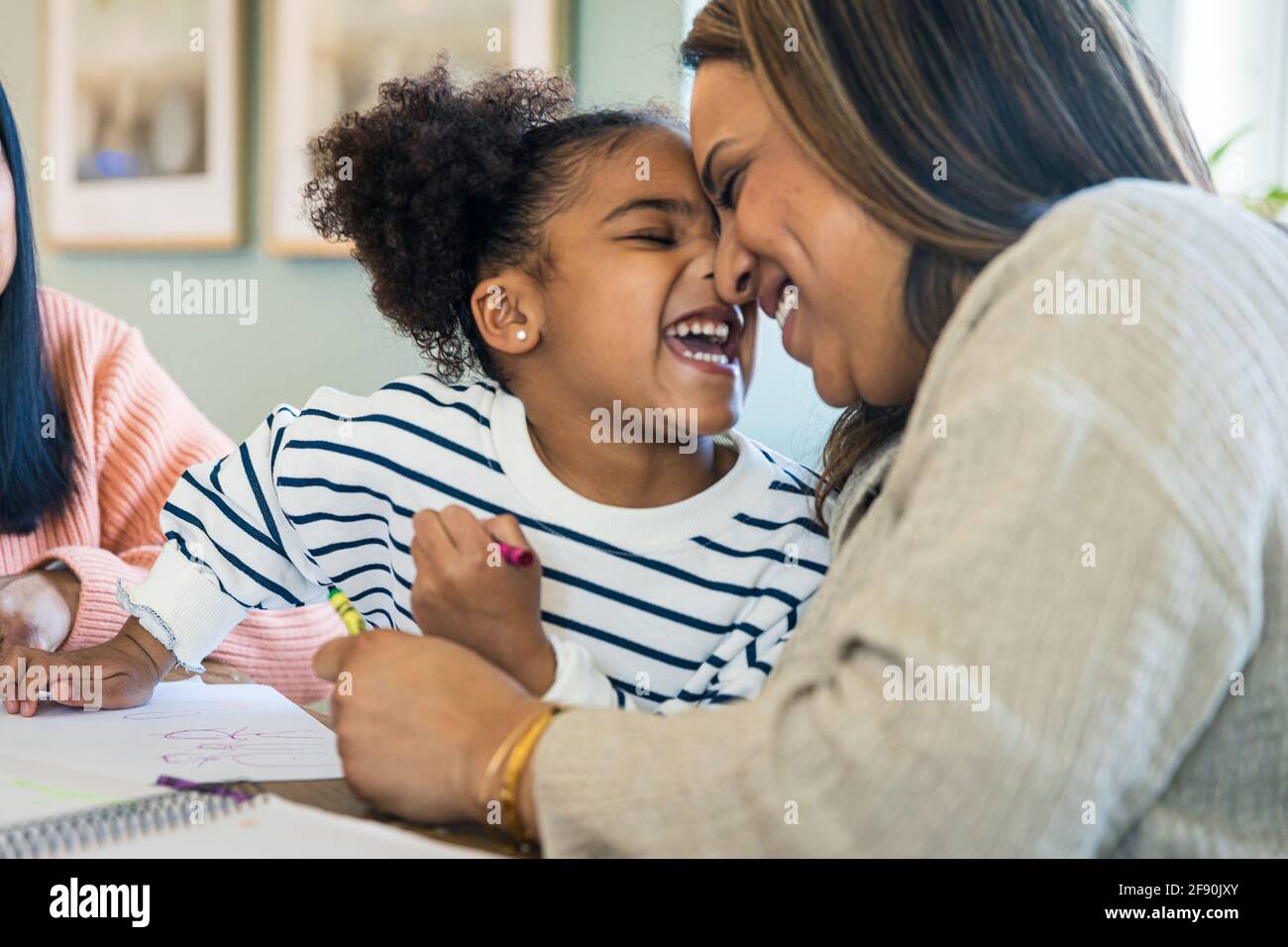Cheerful daughter rubbing nose with mother while learning drawing at home Stock Photo