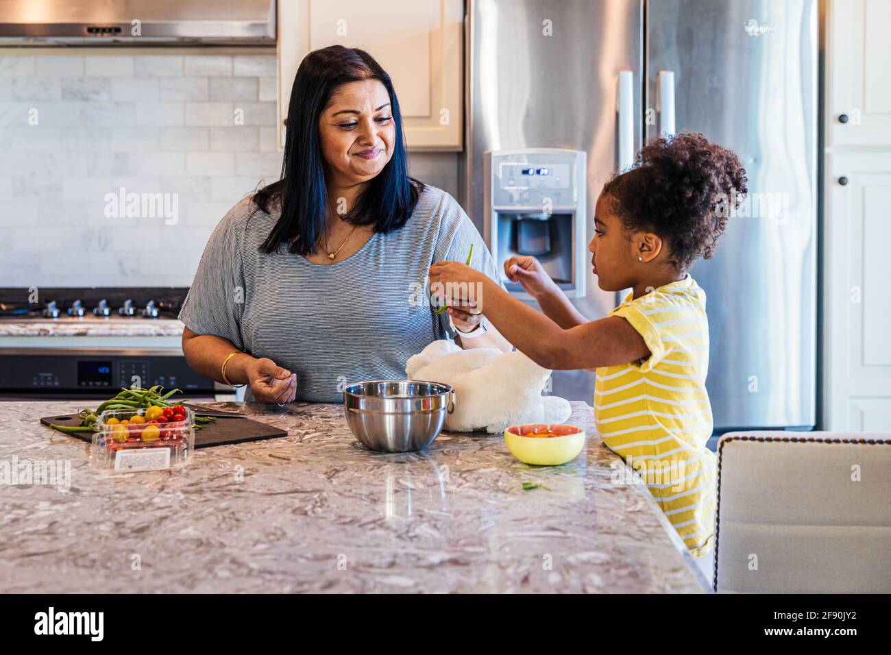 Granddaughter helping grandmother in preparing food at kitchen island Stock Photo