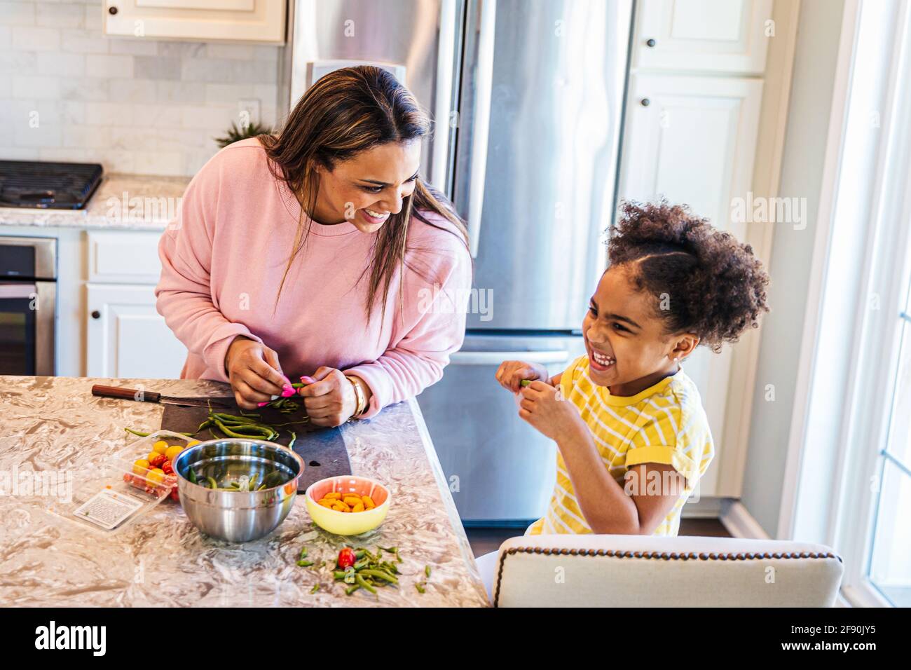 Smiling daughter helping mother in preparing food in kitchen at home Stock Photo