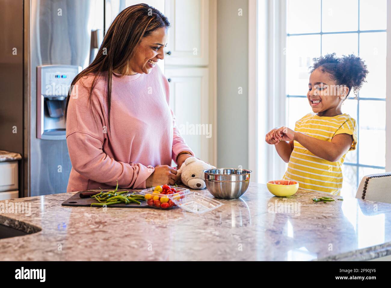 Cheerful daughter helping mother in preparing food at home Stock Photo