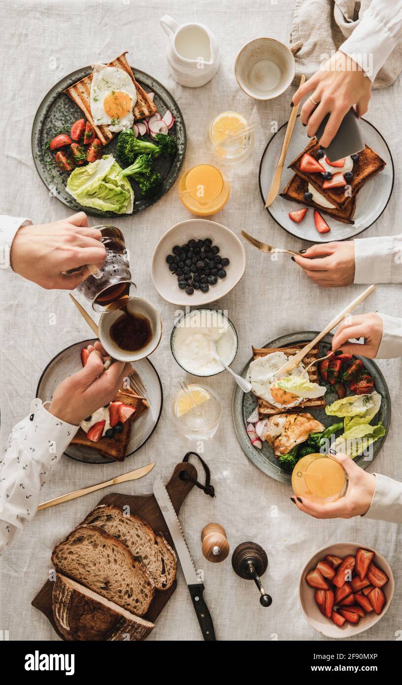 Family having breakfast or gathering dinner together. Flat-lay of table with French toasts, fried egg, fresh bread, veggies, berries and peoples hands Stock Photo