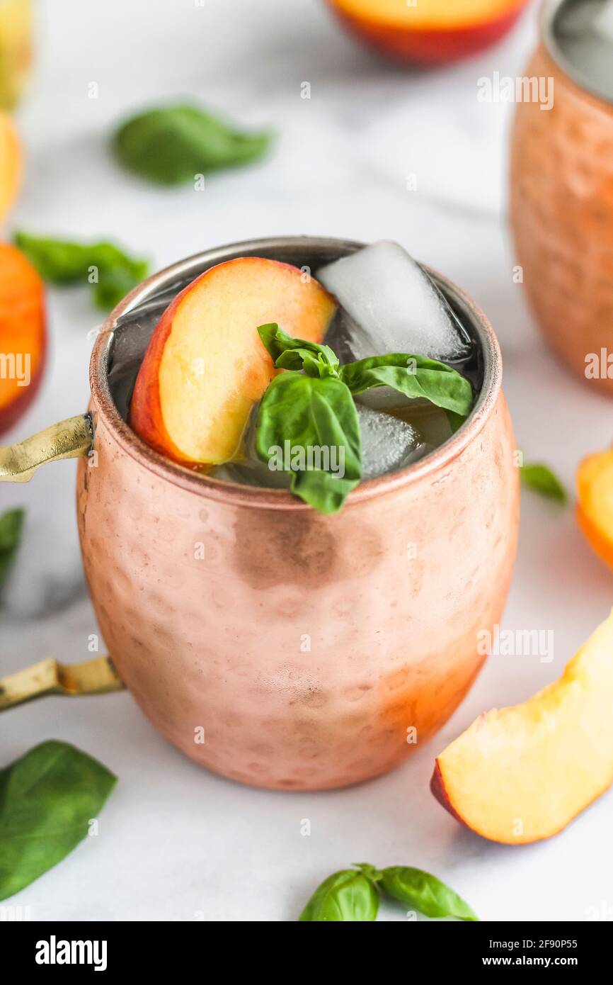 Moscow mule garnished with peach slice and basil leaves Stock Photo