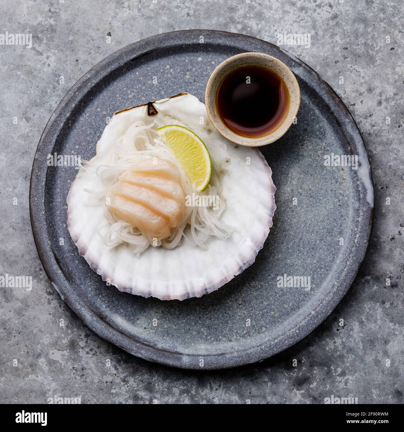 Live scallop sashimi on shell with daikon, lime and soy sauce on gray