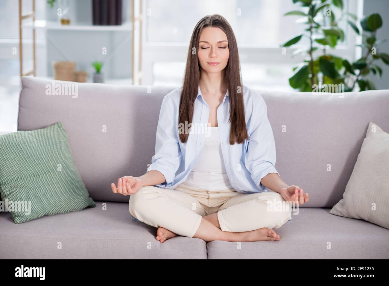 Full size photo of nice optimistic brunette long hairdo lady sit on coach wear blue shirt at home Stock Photo