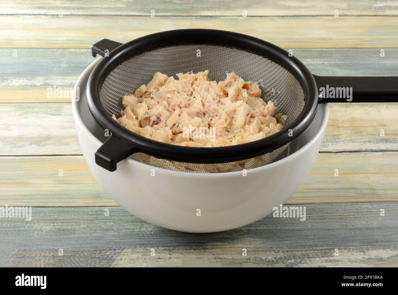 Rinsed canned albacore tuna draining in strainer into white bowl Stock Photo
