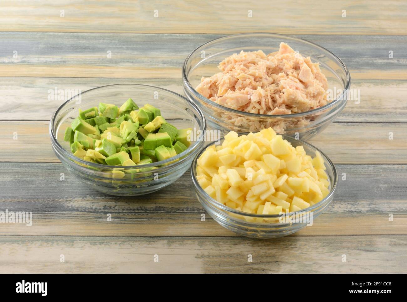 Chopped avocado, apple and albacore tuna soaked in glass ingredient bowls for preparing tuna salad Stock Photo