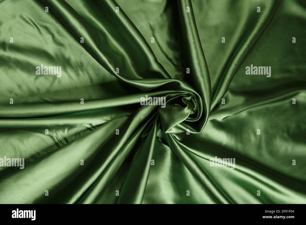 Colored green textile satin fabric folded in folds and waves with highlights and texture shimmers in the light Stock Photo
