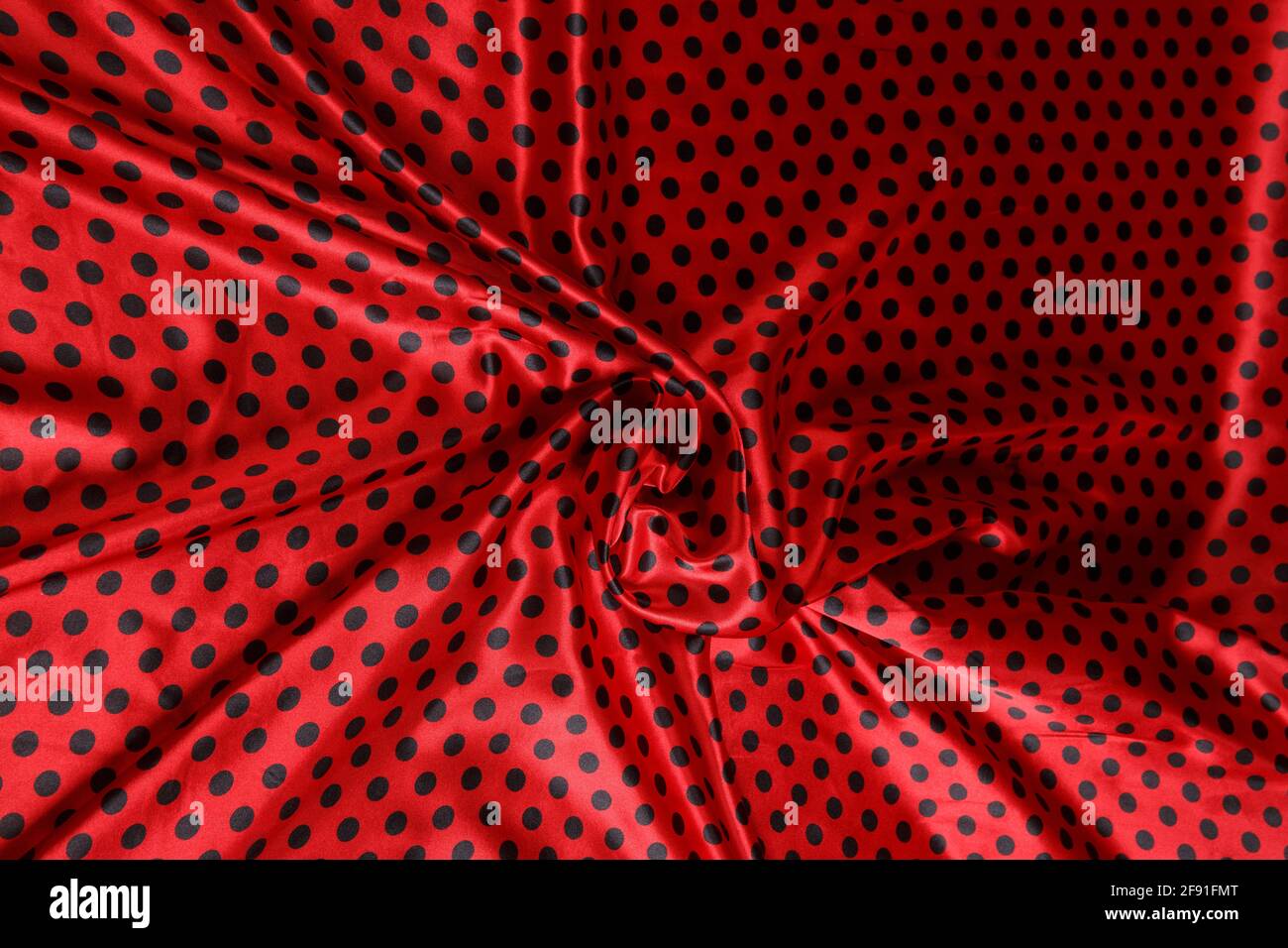Colored red polka dotted textile satin fabric folded in folds and waves with highlights and texture shimmers in the light Stock Photo