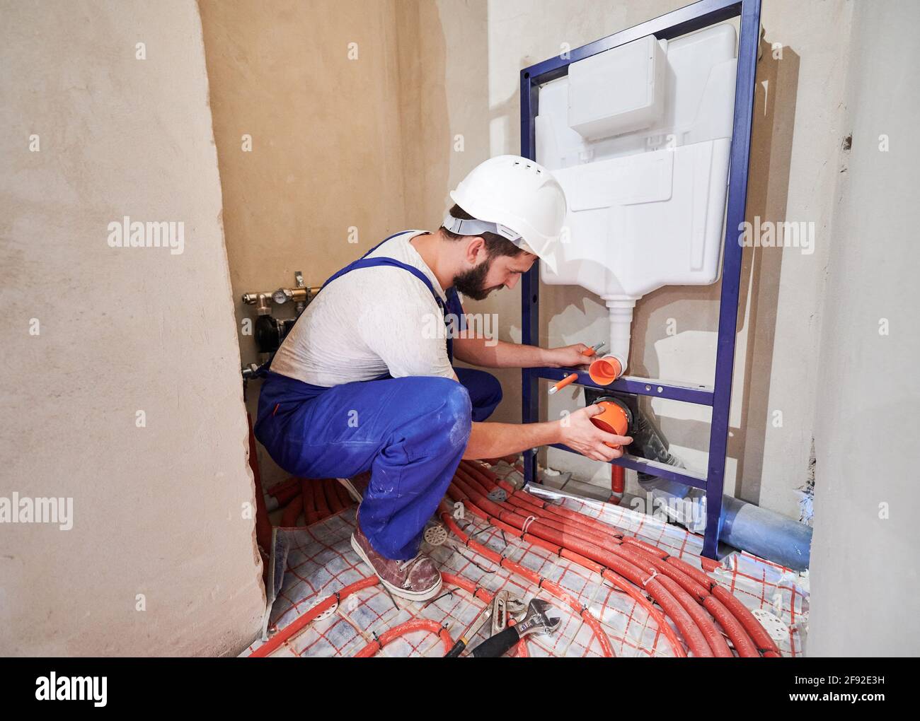 Plumber in work overalls installing concealed toilet frame in bathroom