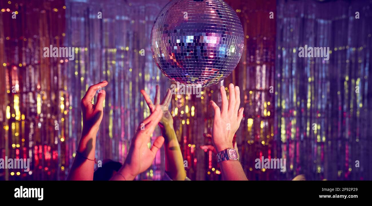 Crowd of people with hands in the air on the dance floor dancing underneath a disco ball. Stock Photo