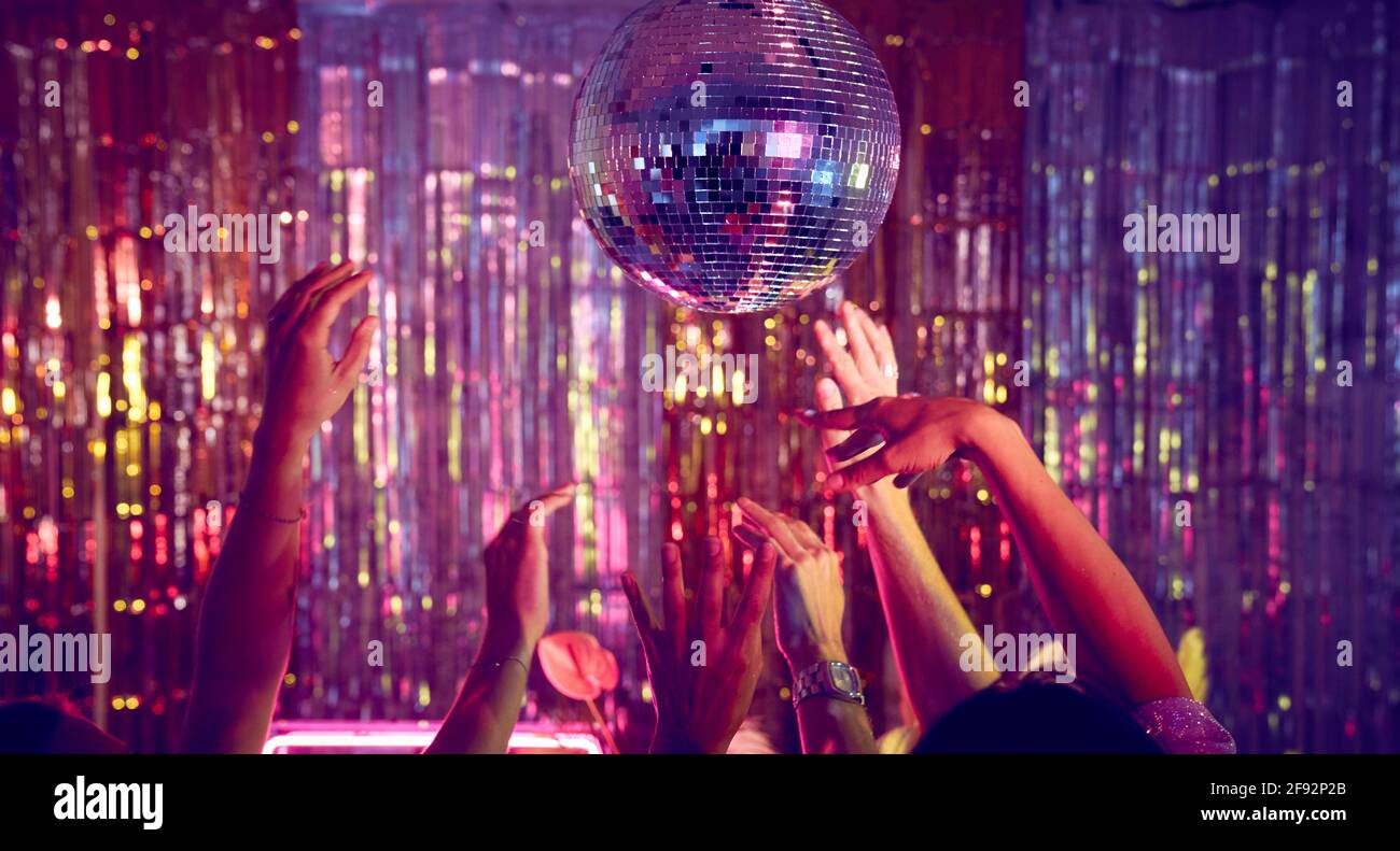 Hands in the air on the dance floor with a sparkly disco ball. Stock Photo