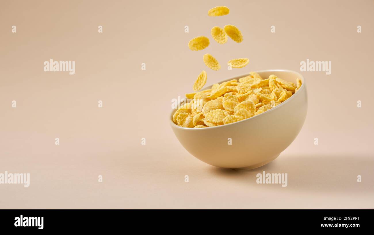 Traditional breakfast with cornflakes. Cornflakes falling into a bowl on a light beige background. Stock Photo