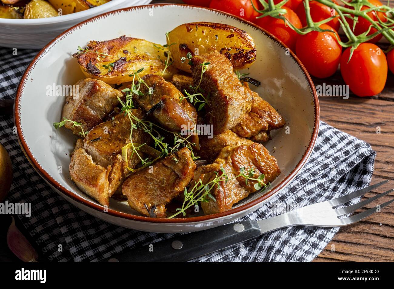 Appetizing stew of pork tenderloin meat cooked in the wok, cut into cubes. With roasted and golden potatoes, garlic, salt, oregano and fresh tomatoes. Stock Photo
