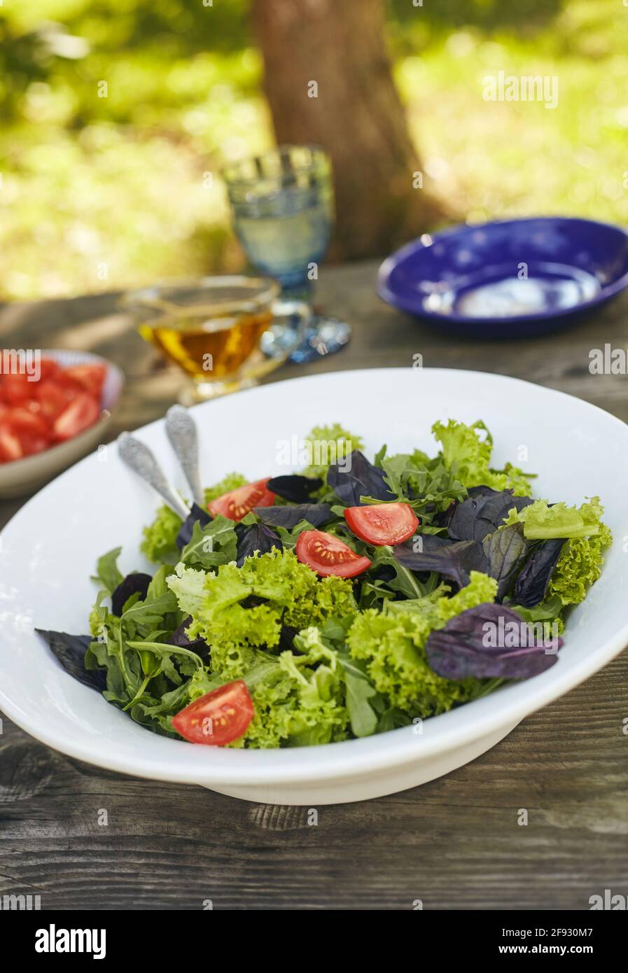 Fresh salad mix of arugula leaves, basil, lambs lettuce and tomatoes. Salad bowl, healthy food. Composition in a white plate on an old wooden table Stock Photo