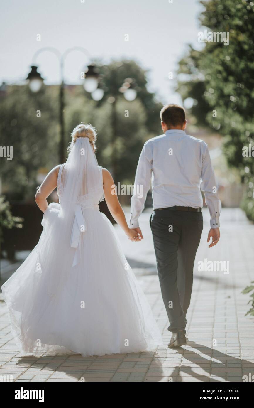 Beautiful view of the bride and the groom walking in the park while ...