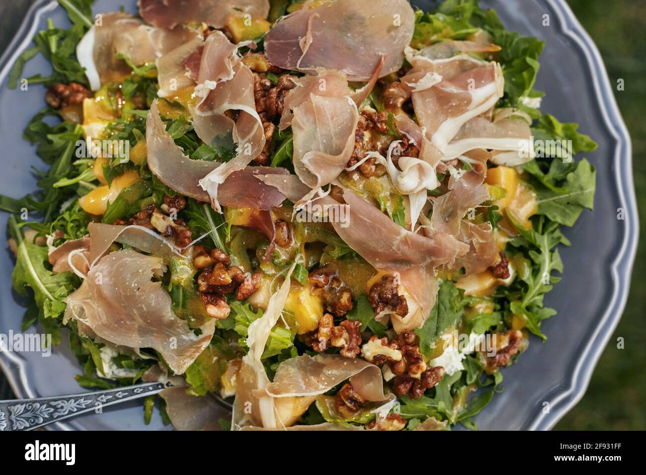 A wonderful salad of arugula, blue cheese, prosciutto, pear and caramelized nuts on a gray stylish plate . Top view Stock Photo
