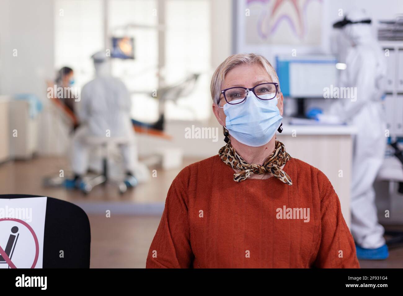 Senior woman in dental clinic wearing face mask looking at camera wainting for consultation during global pandemic with coronavirus. Concept of new normal dentist visit in covid-19. outbreak. Stock Photo