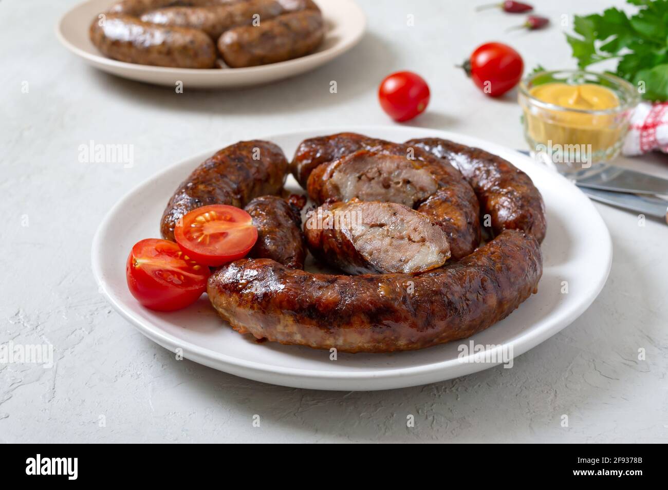 Juicy homemade baked sausage on a plate with mustard and fresh tomatoes. Stock Photo