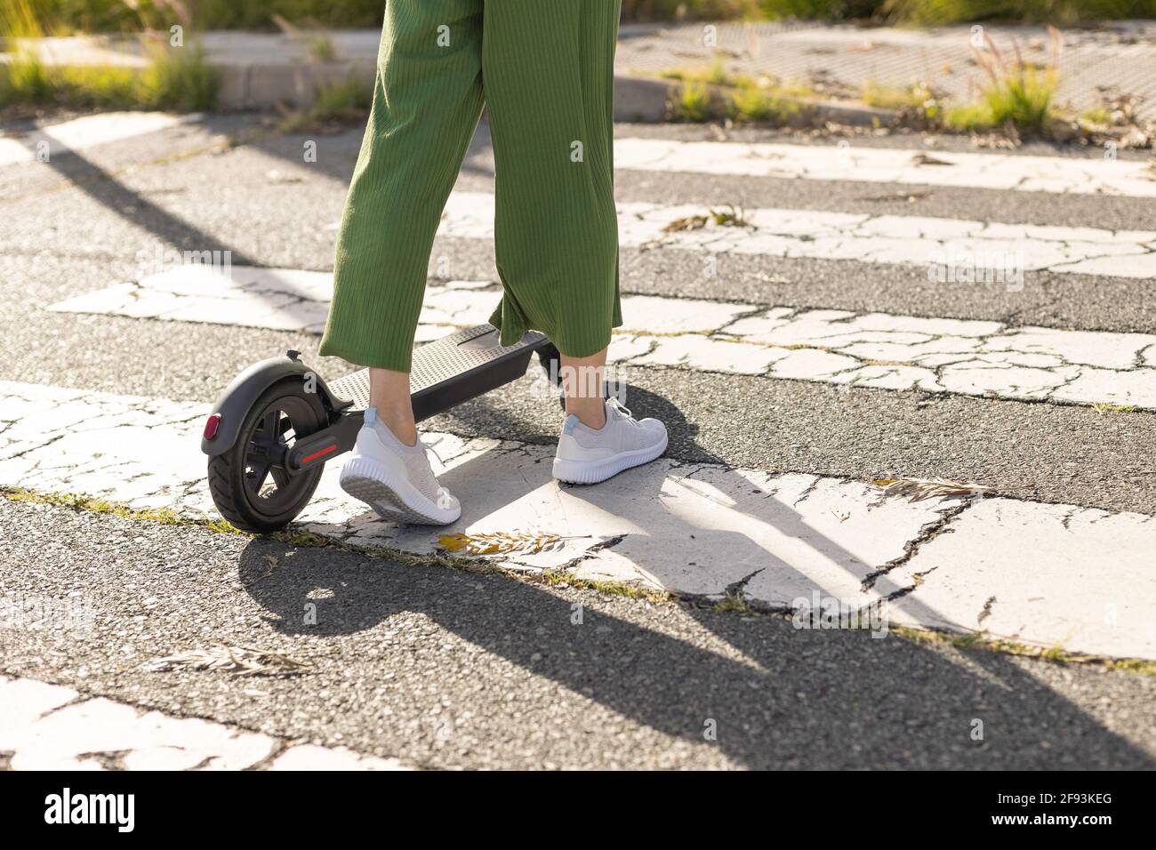Unrecognisable woman on electric scooter crosses street Stock Photo