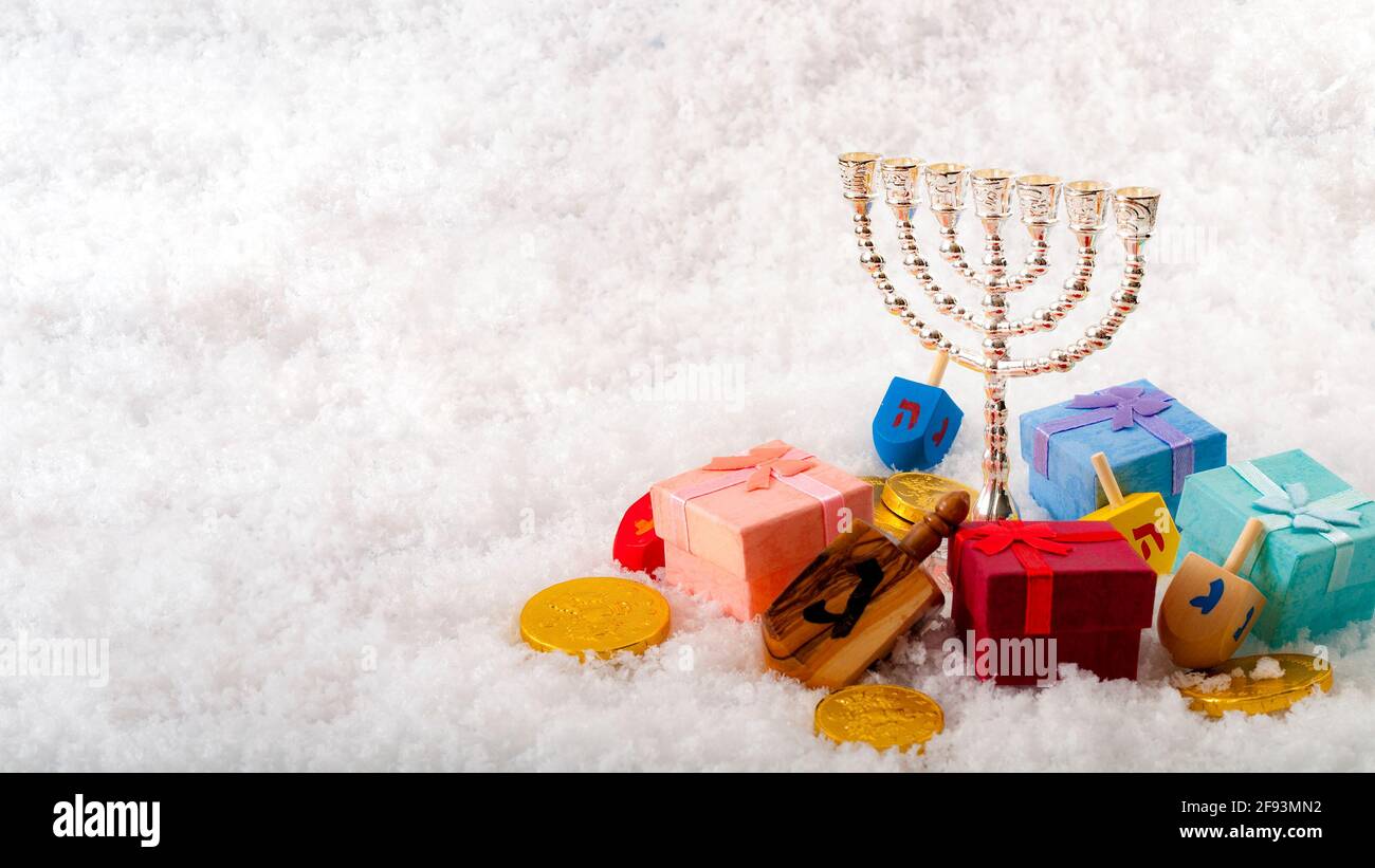 Jewish holiday and Hanukkah celebration with menorah, dreidel, gold coins or gelt and gifts on snow with copy space Stock Photo