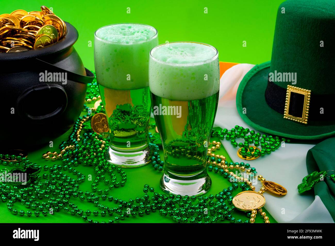 The luck of the Irish meme and Happy St Patricks day concept theme with two glasses of dyed beer, leprechaun hat, beads necklace and pot of gold coins Stock Photo
