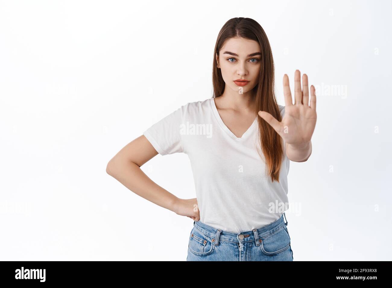 Stop, stay back. Serious and confident girl stretch hand to say no, prohibit, keep social distancing on pandemic, making block gesture, refuse or Stock Photo