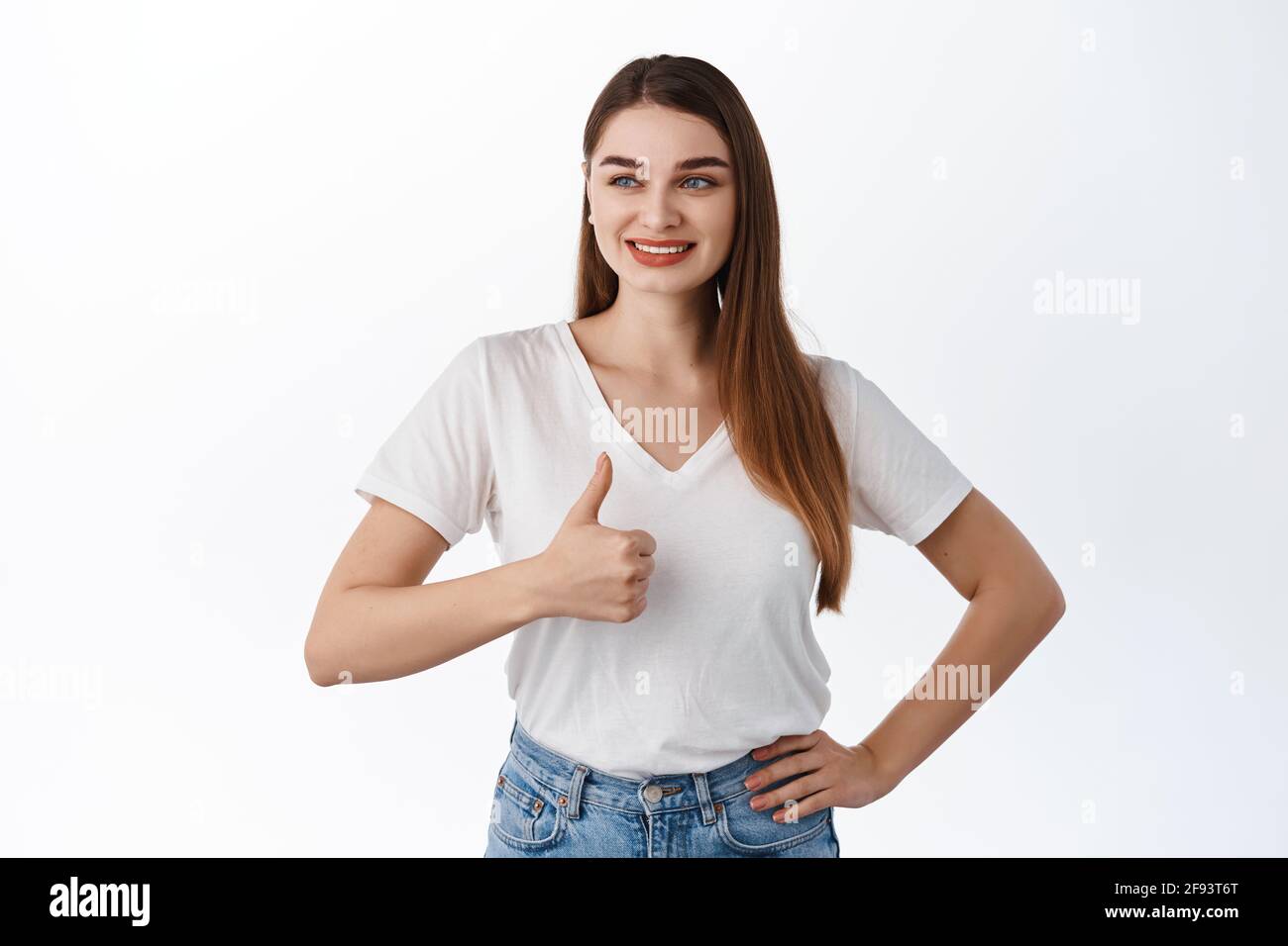 Very good. Smiling young woman looking aside at promo offer and shows thumbs up in approval, praise good shop deal, nice advertisement, satisfied with Stock Photo