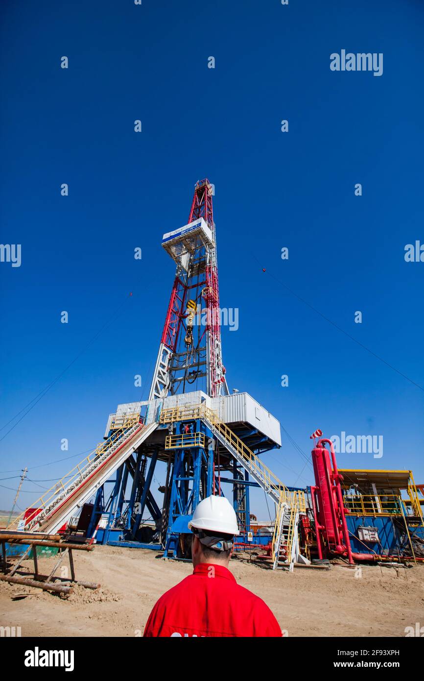 Extraction of oil from deposit with drilling rig. Oil worker in red