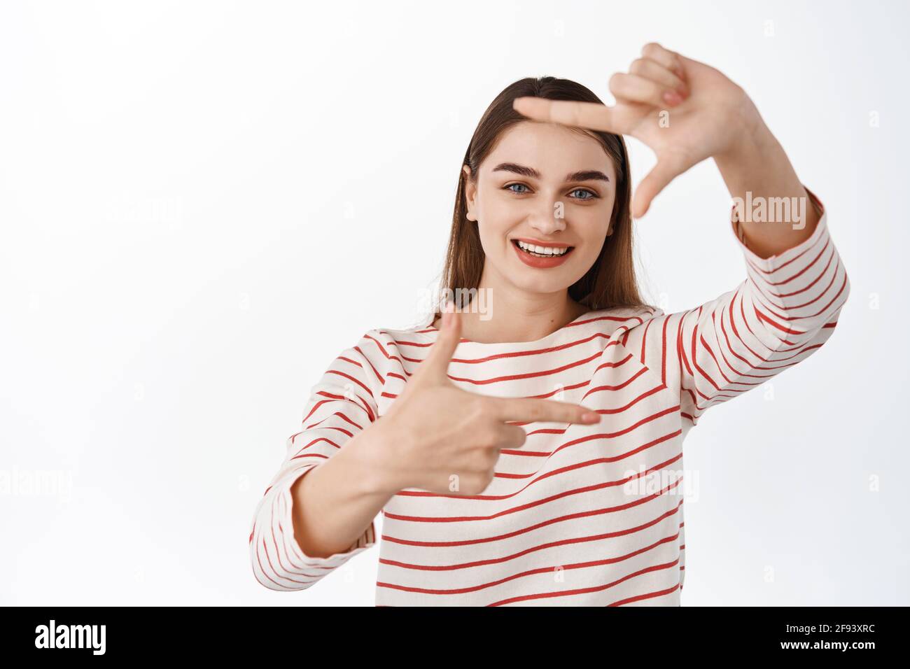 Taking photo to remember. Smiling creative girl show finger hand frames gesture as if taking shot on camera, photographing, looking for perspective Stock Photo