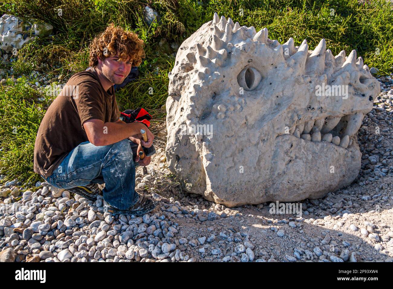 An artist creates a dinosaur head he hews out of a chalk rock on the Jurassic Coast in Beer, England Stock Photo