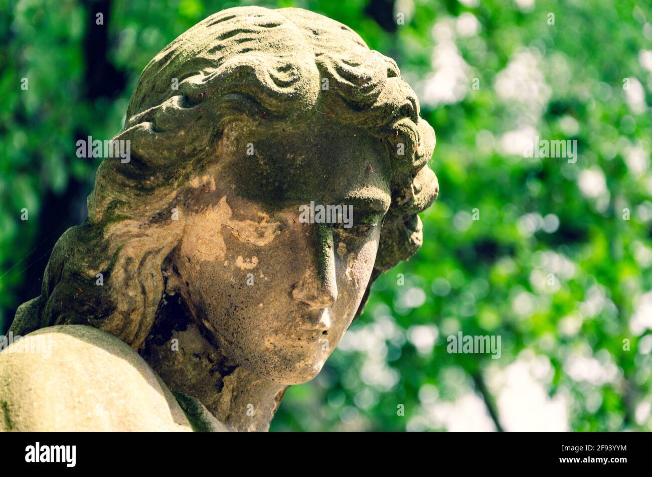 Weathered statue of an Angel with cracked dirty face at old cemetery - cross processed Stock Photo