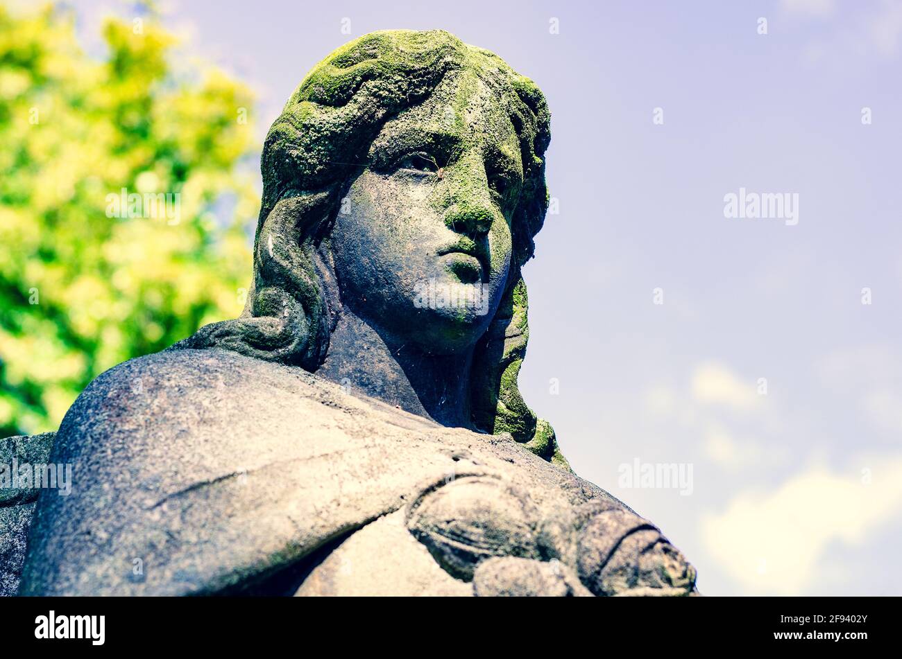 Weathered statue of an Angel with cracked dirty face (with a spider) covered with moss at old
