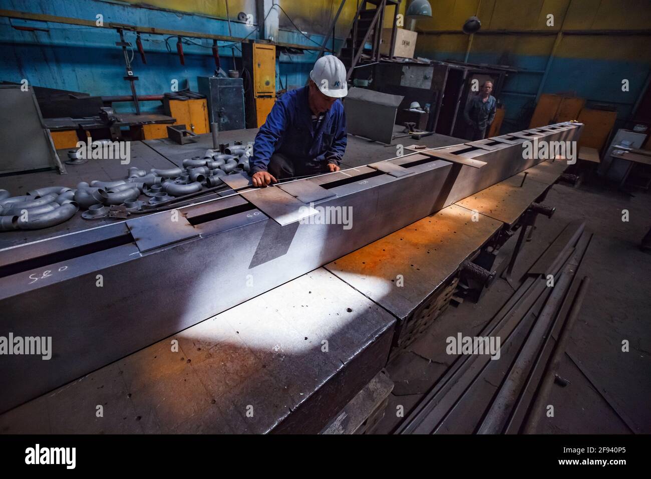 Worker and large metal part. Mechanical workshop. Preparing for welding. Stock Photo
