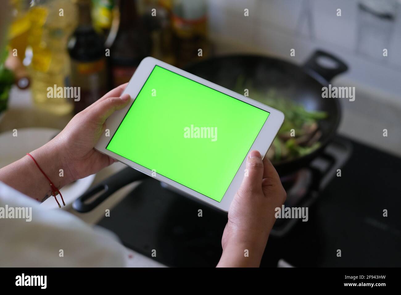 over shoulder view of woman holding green screen tablet when cooking in the kitchen Stock Photo