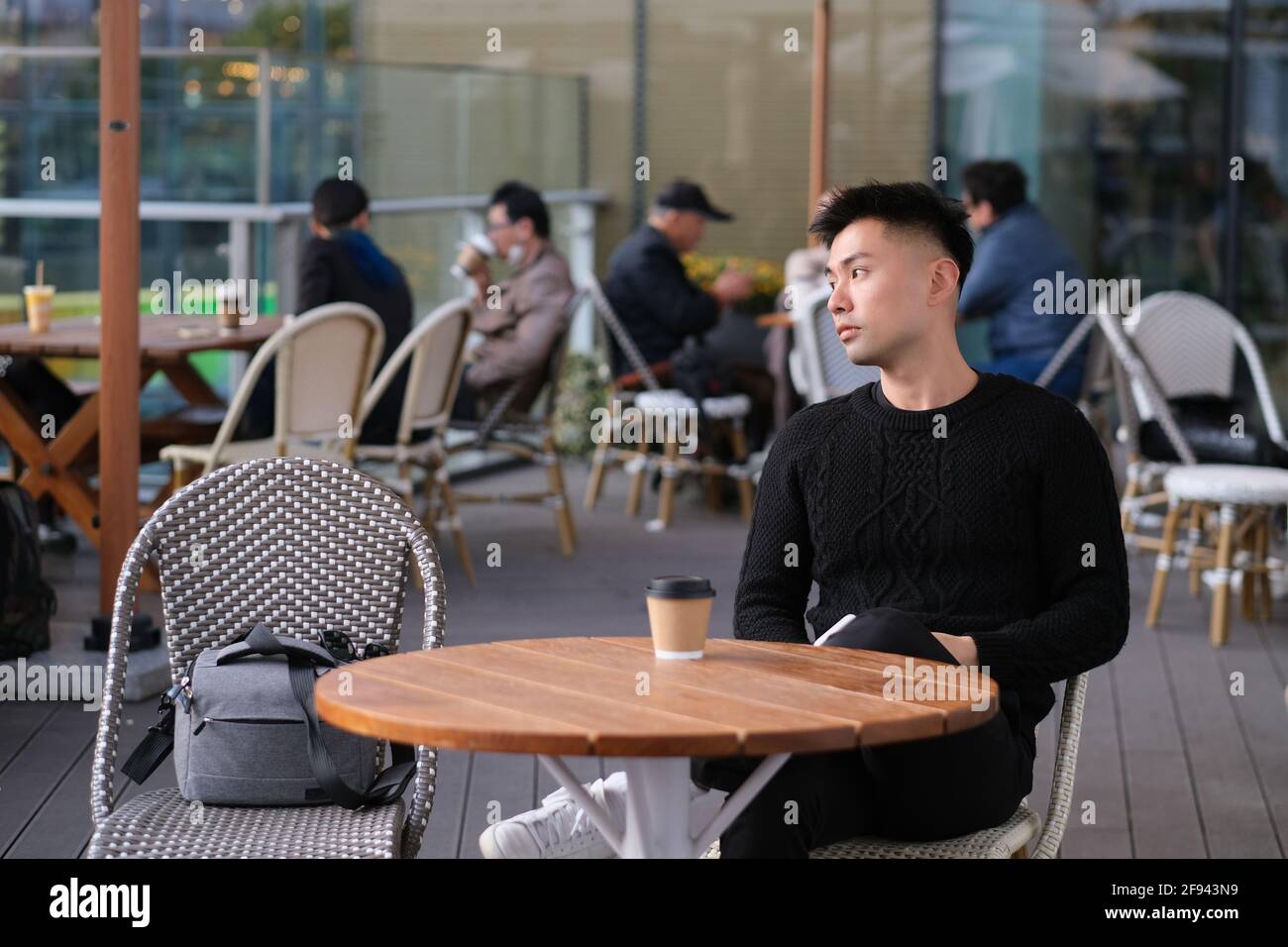handsome Asian young man sitting at open-air cafe, side face looking away Stock Photo