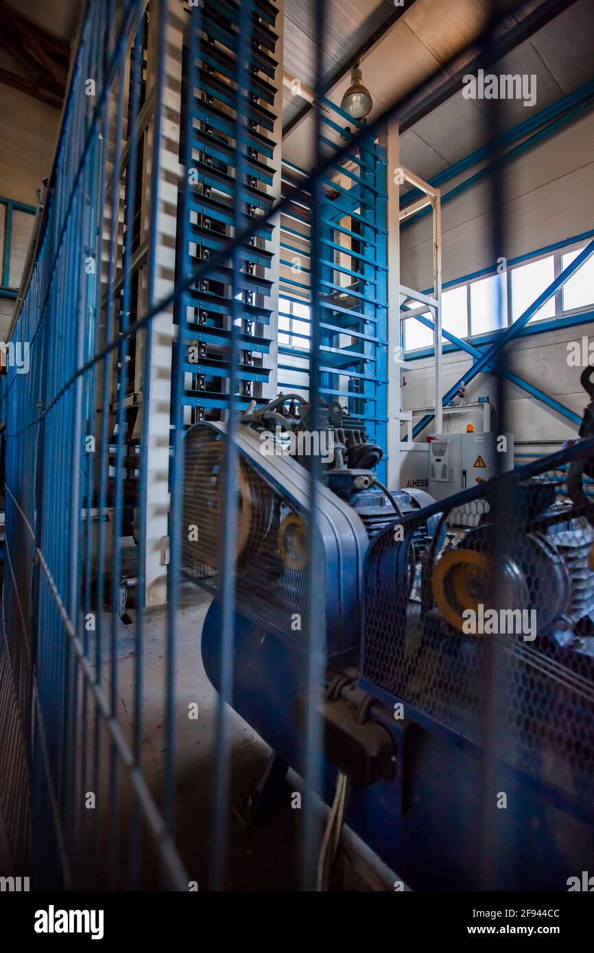 Paving tile production machine. Lifting equipment for tiles packing. Blurred fence on foreground. Stock Photo